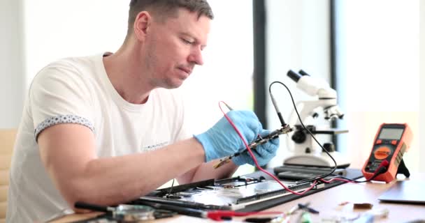 集中型の男は、ワークショップで壊れたラップトップのプリント回路基板を修正します。修理サービスセンタースローモーションで熟練したマスター作品 - 映像、動画