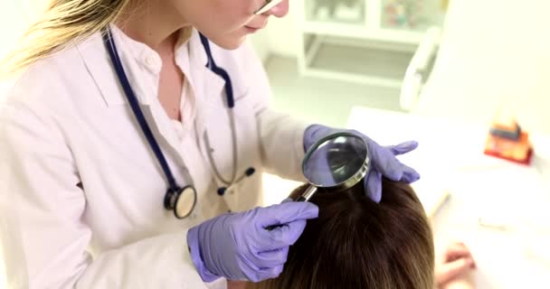 El dermatólogo enfocado mira el cuero cabelludo del paciente a través de una lupa. Especialista trata de encontrar la razón de la pérdida de cabello de la mujer de cámara lenta - Imágenes, Vídeo