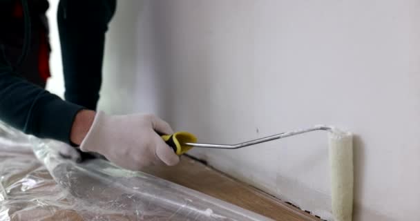 Specialista in guanti protettivi dipinge pareti di colore bianco con rullo. Il caposquadra tratta la parte più bassa di parete in appartamento. Processo di ristrutturazione - Filmati, video