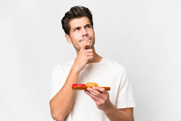 Young caucasian man holding sashimi over isolated white background having doubts and thinking - Фото, зображення