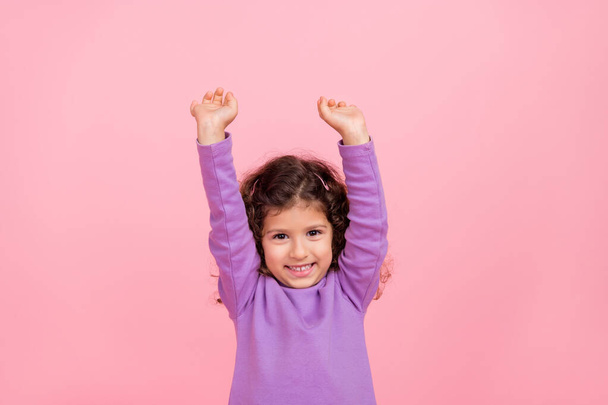 Photo of adorable excited small kid wear violet sweater rising fists isolated pink color background. - Foto, Imagem