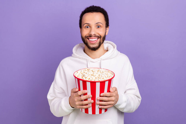 Portrait of cheerful nice person hands hold big popcorn bucket beaming smile isolated on purple color background. - Foto, imagen