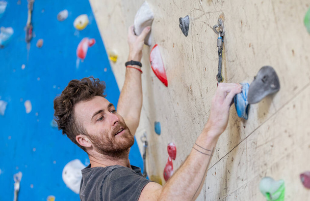 Young man climbing on the indoor climbing wall with a chalked hands - Photo, Image
