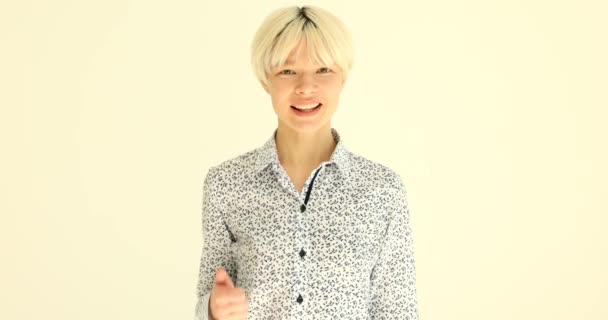 Satisfied woman with dyed blonde hair shows thumb up gesture with hand. Positive lady shows approval looking in camera and smiling slow motion - Footage, Video