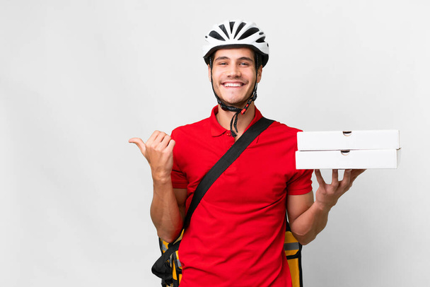 Pizza delivery man with work uniform picking up pizza boxes over isolated white background pointing to the side to present a product - Foto, Imagem