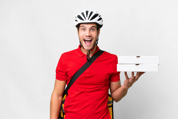 Доставщик пиццы в рабочей форме собирает коробки пиццы на изолированном белом фоне с неожиданным выражением лица - Фото, изображение