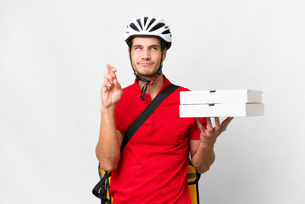 Pizza delivery man with work uniform picking up pizza boxes over isolated white background with fingers crossing and wishing the best - Photo, image