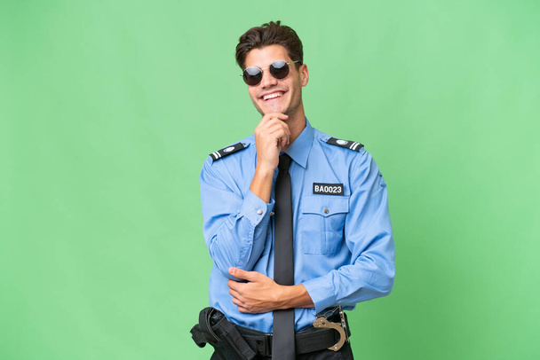Young police man over isolated background with glasses and smiling - Photo, Image