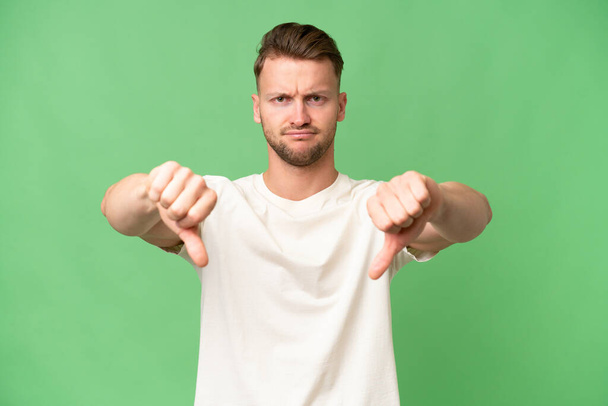 Fiatal szőke fehér férfi izolált háttér mutatja hüvelykujj le két kézzel - Fotó, kép