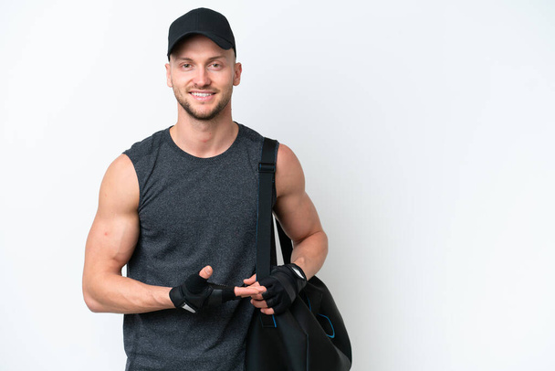Young blonde sport caucasian man with sport bag over isolated white background presenting an idea while looking smiling towards - Fotó, kép