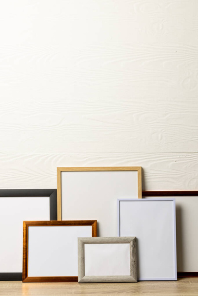 Vertical of six various empty frames with copy space on table against white wall. Mock up frame template, interior design and decoration. - Foto, imagen