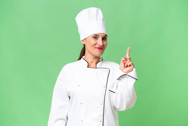 Женщина-повар средних лет на изолированном фоне показывает и поднимает палец в знак лучшего - Фото, изображение