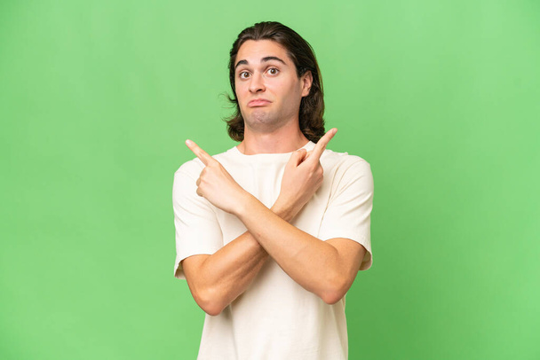 Young caucasian man isolated on green chroma background pointing to the laterals having doubts - Photo, Image