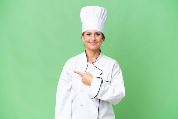 Middle-aged chef woman over isolated background pointing to the side to present a product - Photo, Image