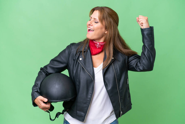 Mulher caucasiana de meia-idade com um capacete de motocicleta sobre fundo isolado celebrando uma vitória - Foto, Imagem