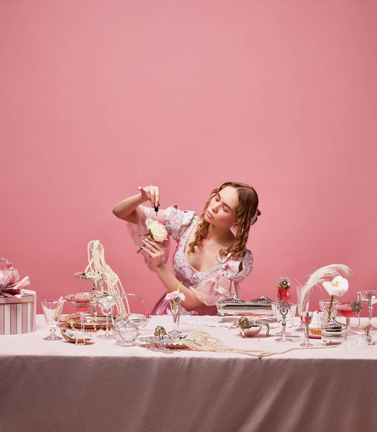 Princesa medieval com rosa. Tiro de menina loira adorável vestindo vestido rosa fantasia e sentado em mesa lindamente colocada sobre o fundo do estúdio. Conceito de medieval, beleza, roupas à moda antiga, anúncio - Foto, Imagem