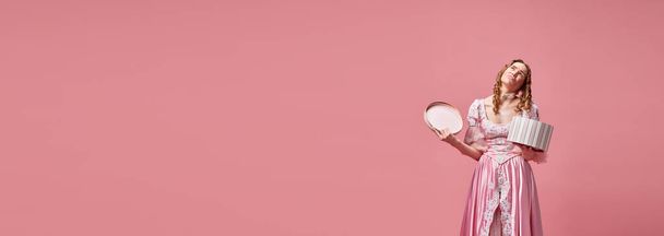 Dislike. Banner with upset, charming, blond princess wearing pink dress and holding gift box with sad face on pink studio background. Concept of medieval, beauty, birthday, human emotions, ad - Photo, Image