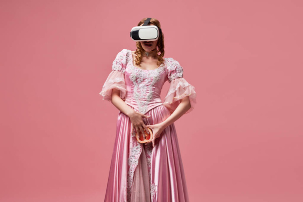 Raus aus dem Problem. Aufnahme einer Prinzessin mit Kleid und Virtual-Reality-Brille, die Grapefruit über rosa Studiohintergrund hält. Konzept von Online, sozialen Netzwerken, Internet, Webcam-Modell - Foto, Bild