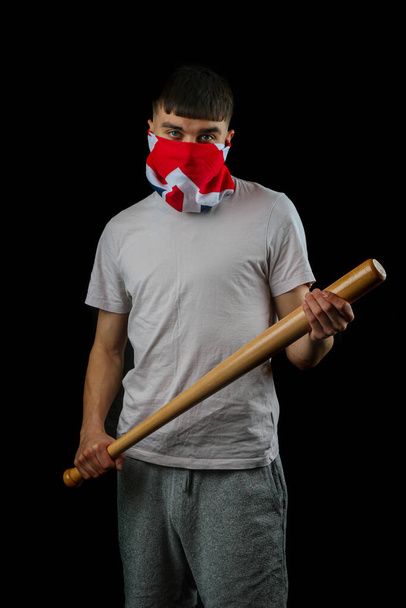 Teenage boy wearing an British flag mask holding a baseball bat against a black background - Photo, image