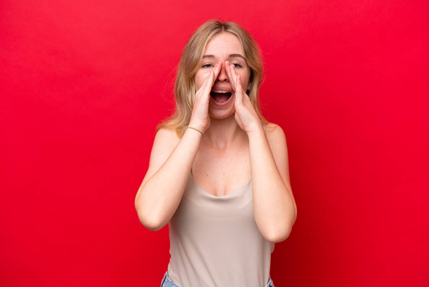 Молодая английская женщина, изолированная на красном фоне, кричит и объявляет что-то - Фото, изображение
