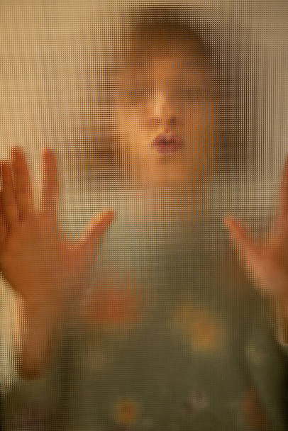 Γυναικείο πορτραίτο μέσα από μια γυάλινη πόρτα στο σπίτι. Γυναίκα που αγγίζει γυάλινη επιφάνεια - Φωτογραφία, εικόνα
