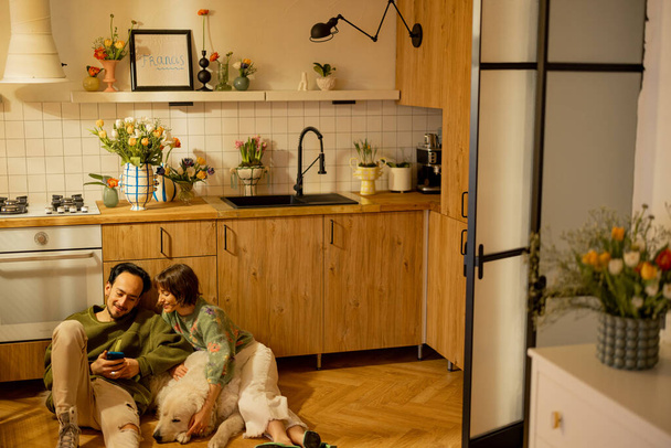Nuori pari istua rento yhdessä söpö koira keittiössä kotona. Koti kodikkuus ja kotimainen elämäntapa käsite - Valokuva, kuva