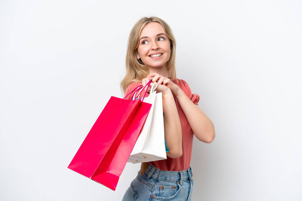 Junge Engländerin isoliert auf weißem Hintergrund mit Einkaufstaschen und lächelnd - Foto, Bild
