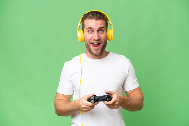 Young handsome man playing with a video game controller isolated on green chroma background - Foto, Imagem