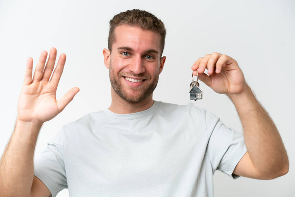 Joven hombre caucásico sosteniendo llaves de casa aisladas sobre fondo blanco apuntando hacia un lado para presentar un producto - Foto, imagen