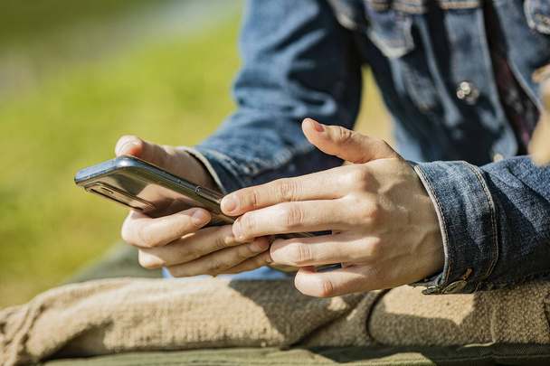 Close-up of a young woman's hands using a smartphone in an outdoor setting. Perfect for technology and lifestyle themes. - Φωτογραφία, εικόνα