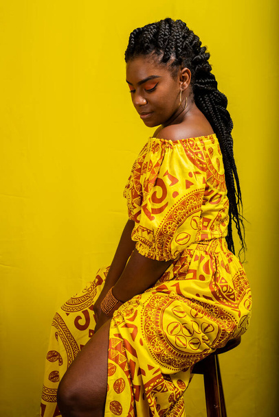 Beautiful young woman sitting on a stool. Colorful clothes. Isolated on yellow background. - Fotoğraf, Görsel