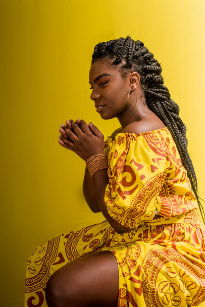 Portret van een mooie vrouw, zittend, met haar handen in de vorm van een gebed. Geïsoleerd op gele achtergrond. - Foto, afbeelding