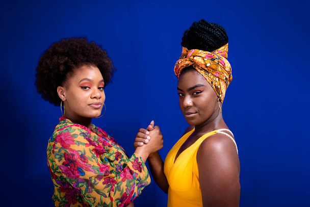 Two women, friends, holding hands looking at the camera against a blue background. - Fotó, kép