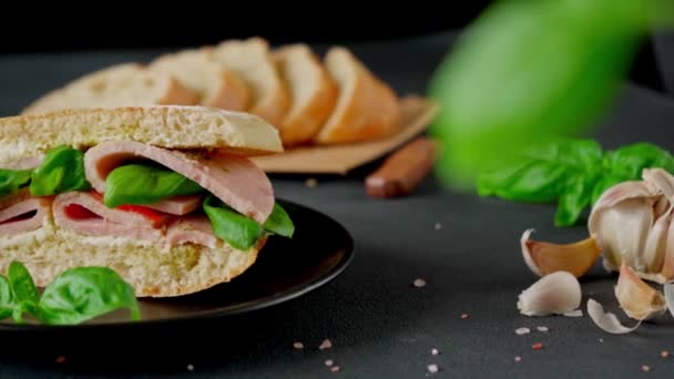 Ciabatta-Sandwich mit Schinken, Pesto-Sauce, Tomaten, Basilikum auf schwarzem Hintergrund. Essen. Lebensmittel-Hintergrund. Nahaufnahme - Filmmaterial, Video