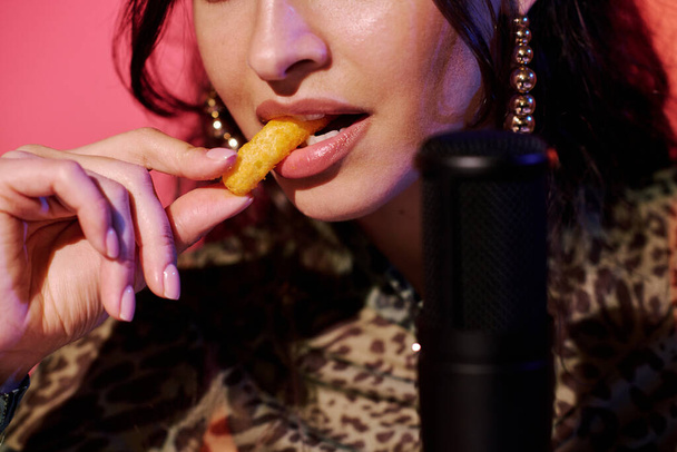 Moderni nuori nainen vaikuttaja istuu studiossa vaaleanpunainen neon valo tallennus rapea maissi puff välipaloja syö ääniä ASMR vlog - Valokuva, kuva