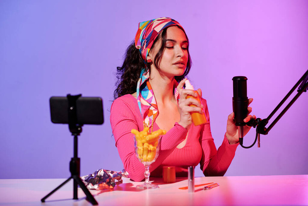 Молодая женщина в модном наряде сидит в студии и записывает ASMR звук распыления чего-то - Фото, изображение
