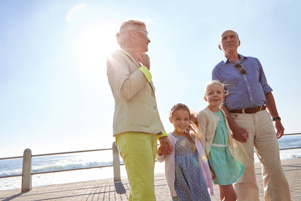 Nuestras bendiciones más grandes nos llaman abuela y abuelo. abuelos caminando de la mano con sus nietas en un paseo marítimo - Foto, imagen