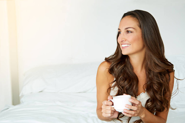 Tomando el sol de la mañana con un café. una joven bebiendo un café en su cama - Foto, imagen
