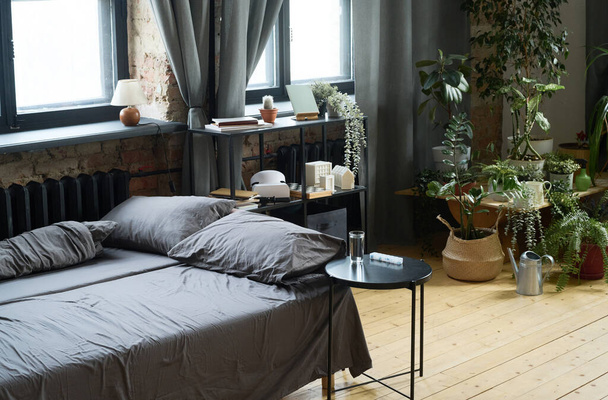 Horizontales Bild eines leeren Bettes mit Zimmerpflanzen im Hintergrund im modernen Schlafzimmer - Foto, Bild