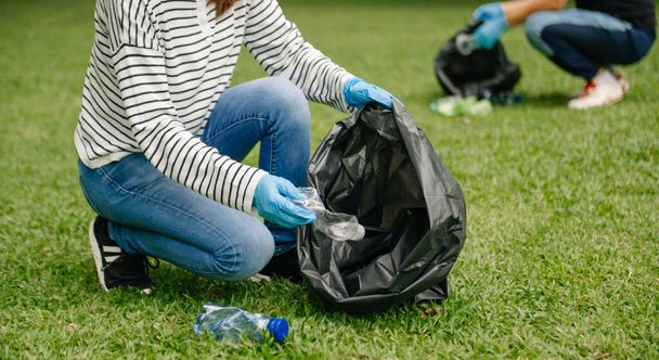 Two people keeping garbage plastic bottles into black bags at park. Clearing, pollution, ecology and plastic concept.  - Foto, imagen