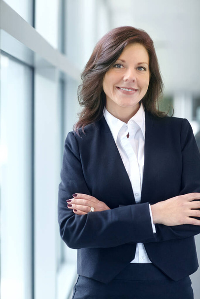 Portrait of a confident businesswoman with arms crossed in a modern office. One smiling professional entrepreneur standing with arms folded wearing a stylish suit. Female lawyer ready for a client. - Foto, Imagem