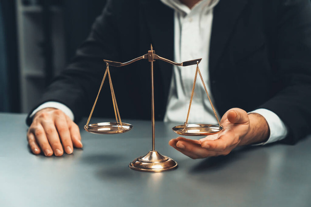 Lawyer in a black suit sits attentively on his office desk with a golden scale balance, symbol of legal justice and integrity, balanced and ethical decision making in the court of law. equility - Photo, Image