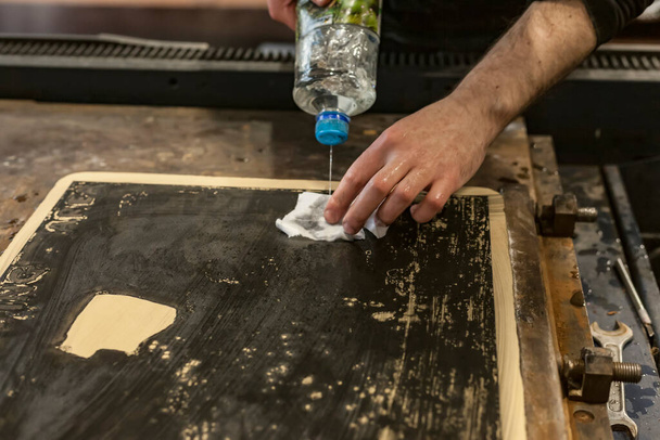 De kunstenaar maakt een lithografische kalksteen schoon met een klonter en chemicaliën in een kunstwerkplaats. - Foto, afbeelding