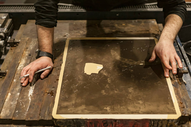 Litografi sanatçısı bir bıçak ya da neşter tutuyor ve taştan bir kireçtaşıyla çalışıyor.. - Fotoğraf, Görsel