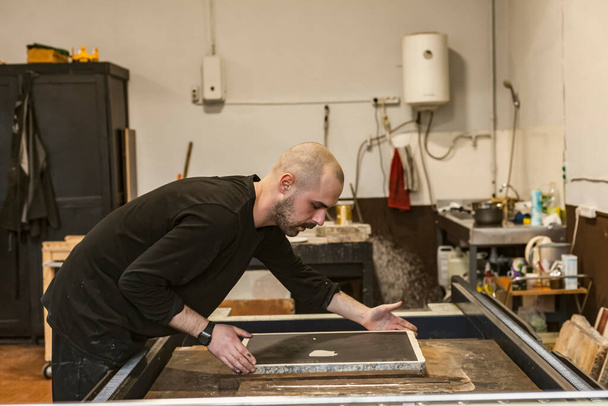 De kunstenaar plaatst een lithografische kalksteen op een lithografische pers of rolpers die wordt gebruikt voor het maken van lithografie in een kunstwerkplaats. - Foto, afbeelding