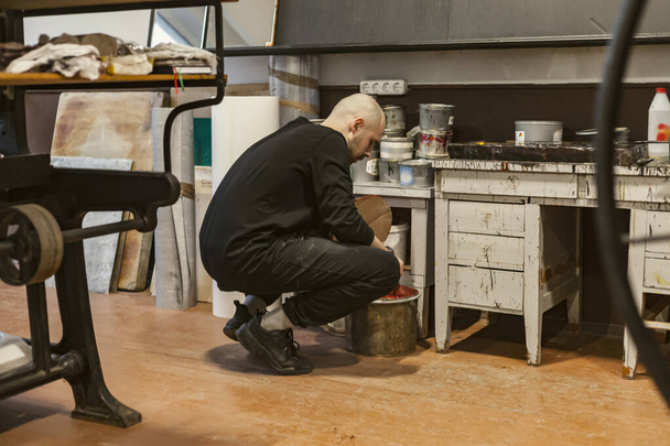 Kunstenaar die verf mengt of neemt in een emmer in een lithografische werkplaats. - Foto, afbeelding
