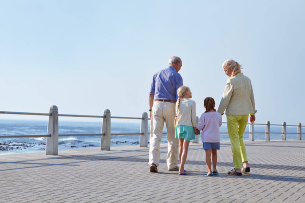 Los abuelos hacen cada día espacial. abuelos caminando de la mano con sus nietas en un paseo marítimo - Foto, imagen