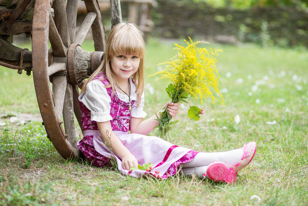 Schöne kleine glückliche Mädchen in einem Kleid und mit einem Strauß gelber Blumen in der Natur im Dorf. Kind im Freien. Mädchen auf einem Spaziergang im Park. - Foto, Bild