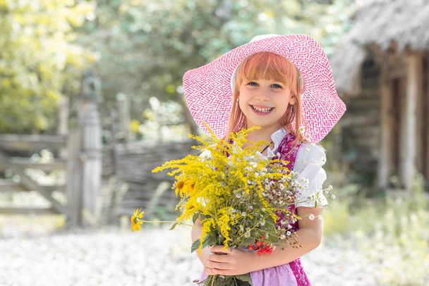 Menina feliz pequena bonita em um vestido e com um buquê de flores amarelas na natureza na aldeia. Criança ao ar livre. Menina em um passeio no parque. - Foto, Imagem