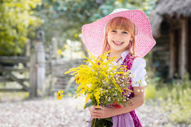 Schöne kleine glückliche Mädchen in einem Kleid und mit einem Strauß gelber Blumen in der Natur im Dorf. Kind im Freien. Mädchen auf einem Spaziergang im Park. - Foto, Bild